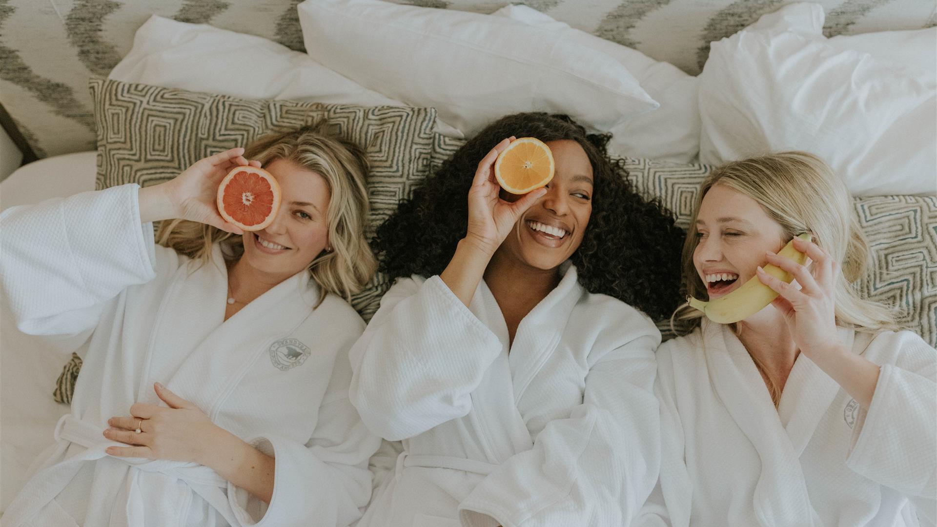 Three women in spa robes smiling and holding fruit