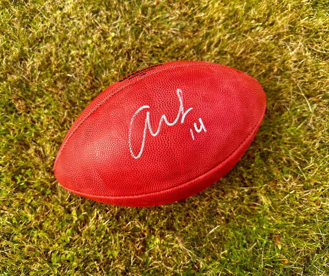 Red football with a signature and the number 14, resting on grass.